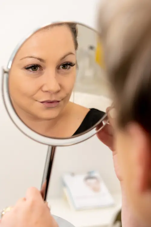 A female examining her reflection in a hand mirror at NiZ Clinic, Gold coast - Australia